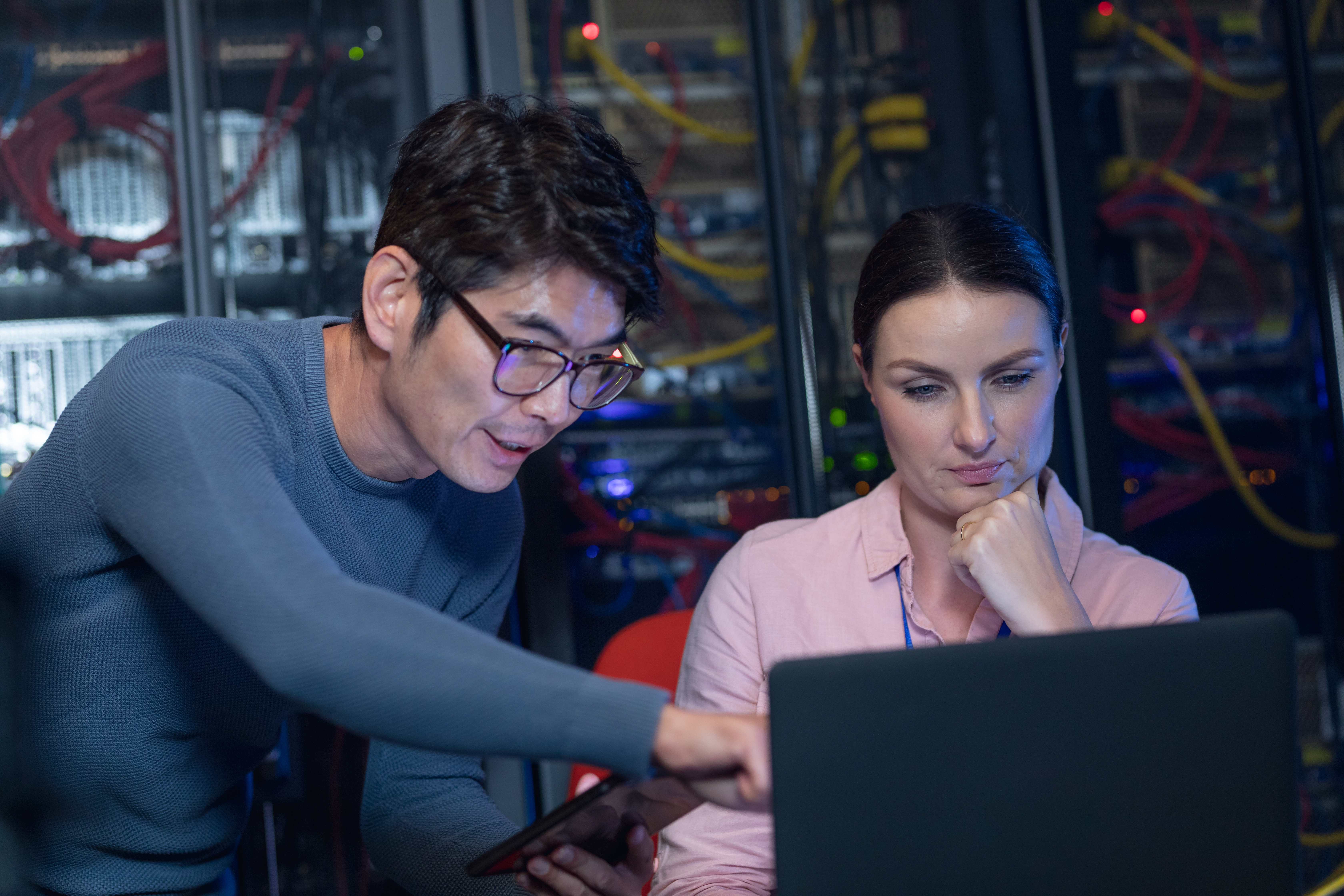 Diverse male and female engineers discussing over a laptop in computer server room