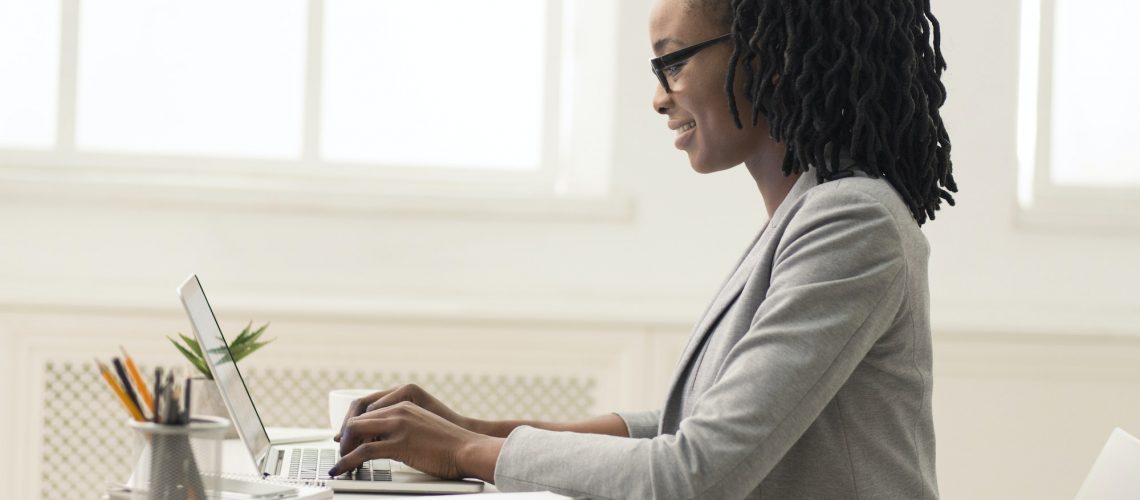 African American Lady Using Laptop In Office, Side View, Panorama