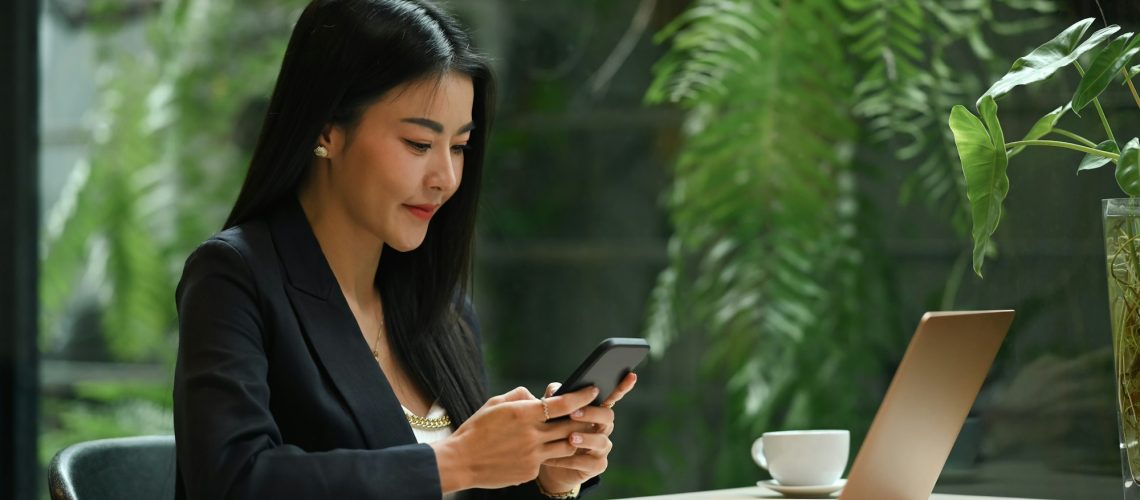 Asian working woman texting text message on her smart phone, working in modern office.