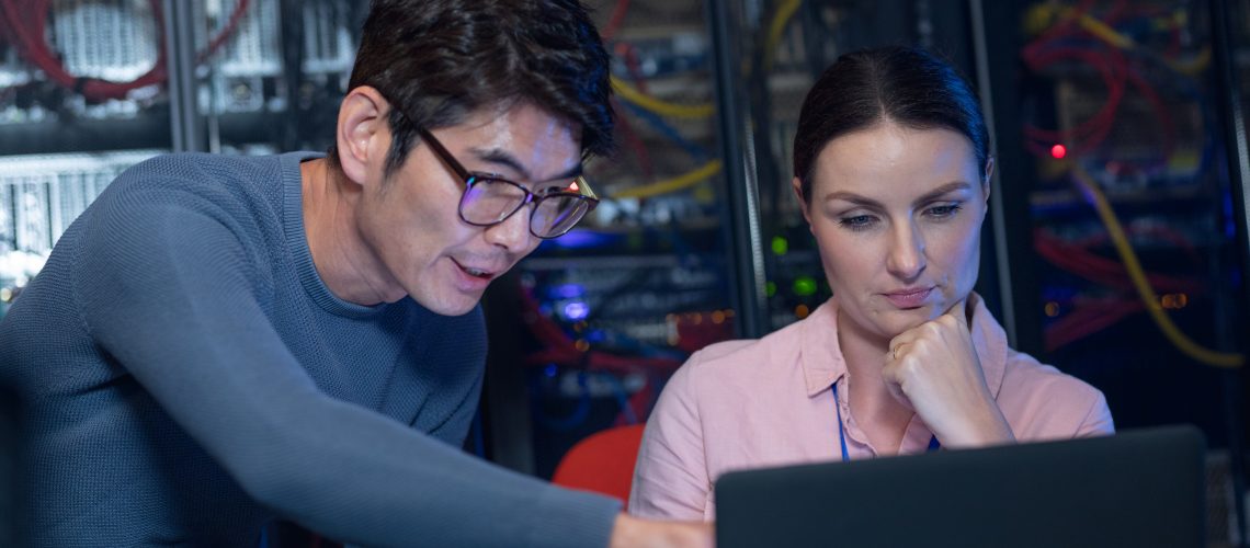 Diverse male and female engineers discussing over a laptop in computer server room