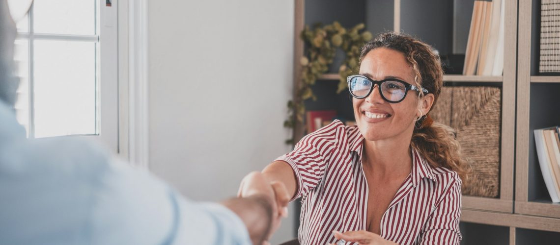 Smiling caucasian female hr manager handshake hire male candidate at job interview